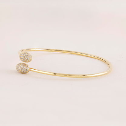 Gold bangle with two diamond-studded ends on a light pink background