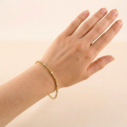 Hand wearing a gold bracelet on a beige background