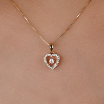 A delicate gold chain necklace with a heart-shaped pendant, worn on a person's neck. The pendant features a double-heart design with a central clear gemstone surrounded by small sparkling stones.