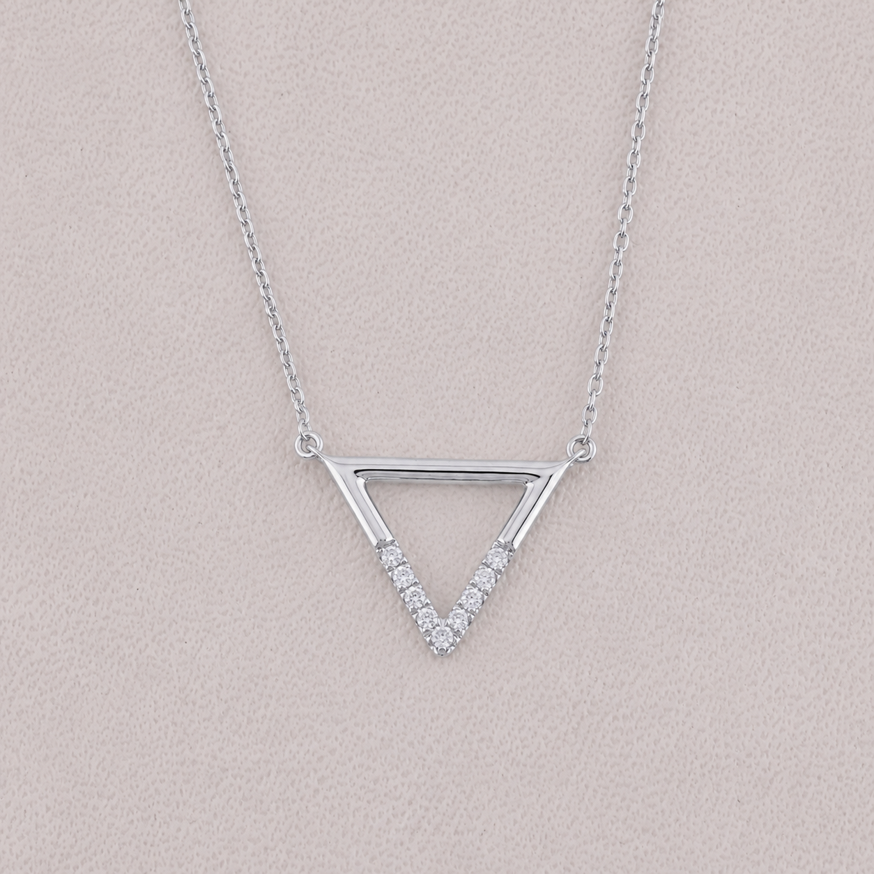 Silver triangle necklace with small diamonds on a light pink background