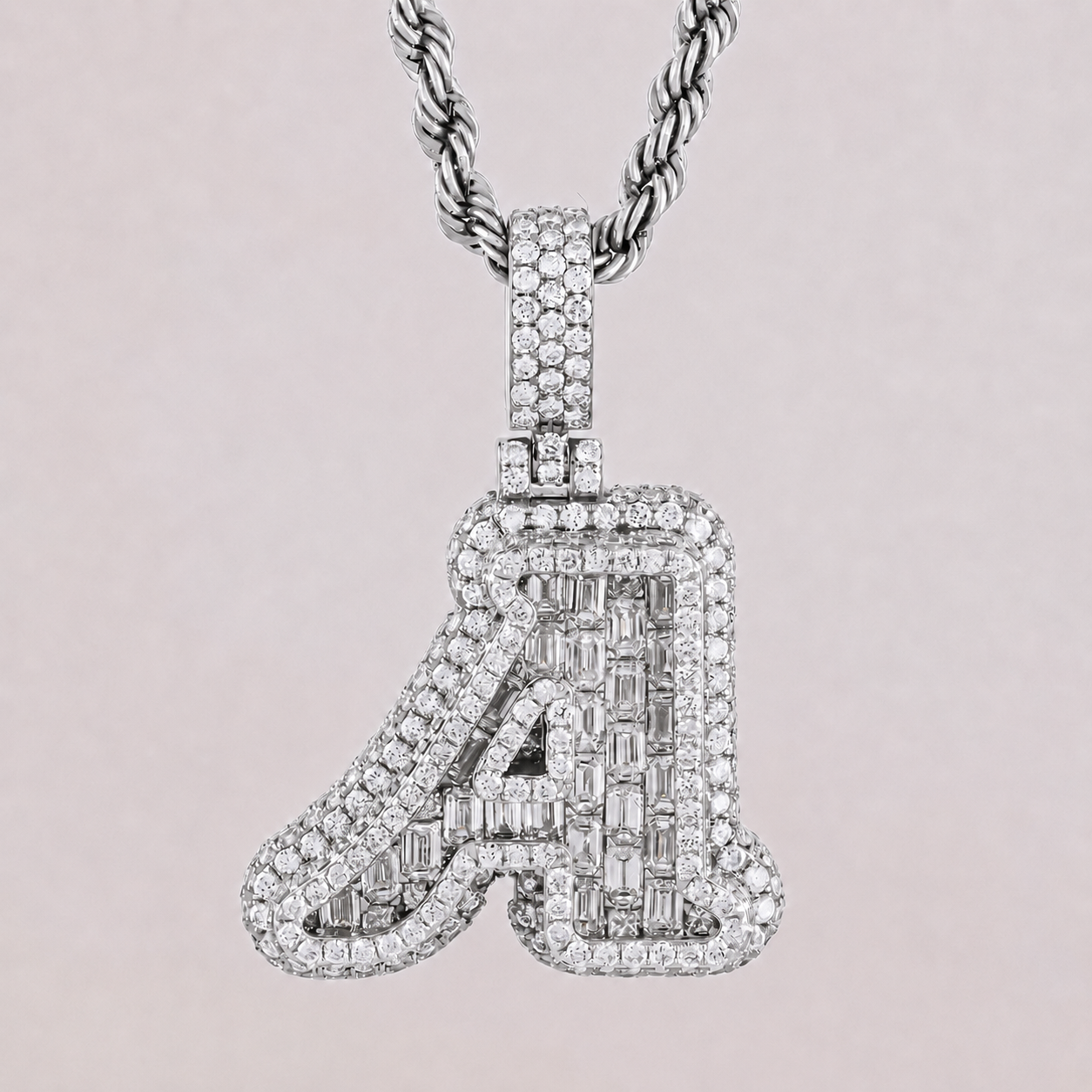 Diamond-studded letter 'A' pendant on a chain against a light pink background