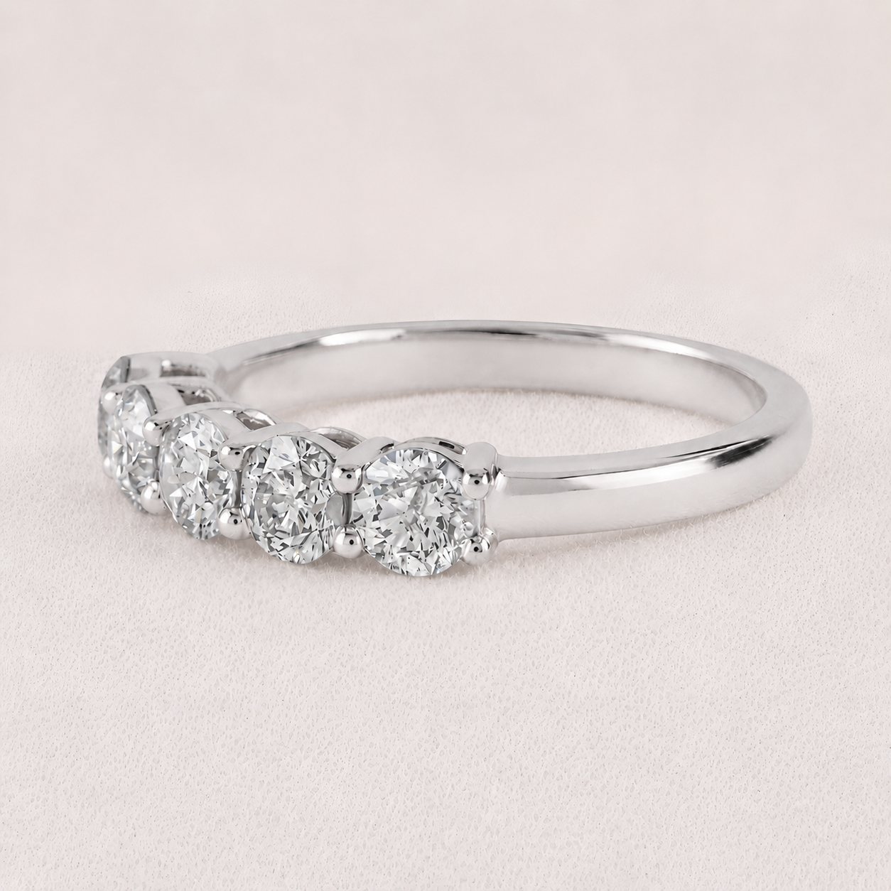 A five-stone diamond ring in a polished silver-colored metal band, set against a soft, light pink textured background.