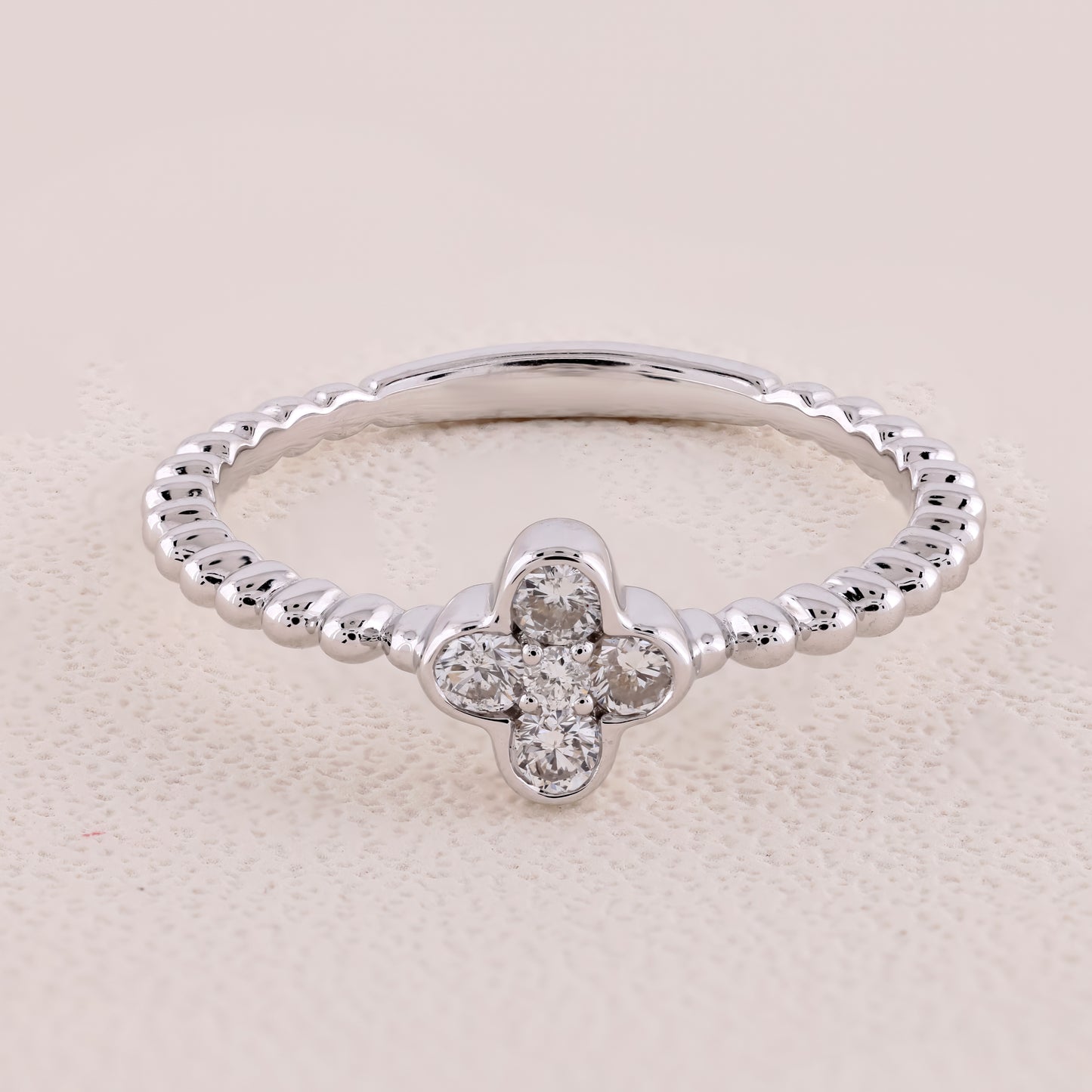 Silver ring with a clover-shaped diamond on a beige background