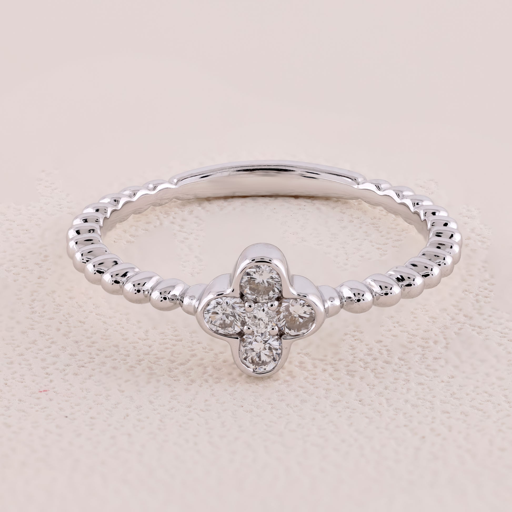Silver ring with a clover-shaped diamond on a beige background