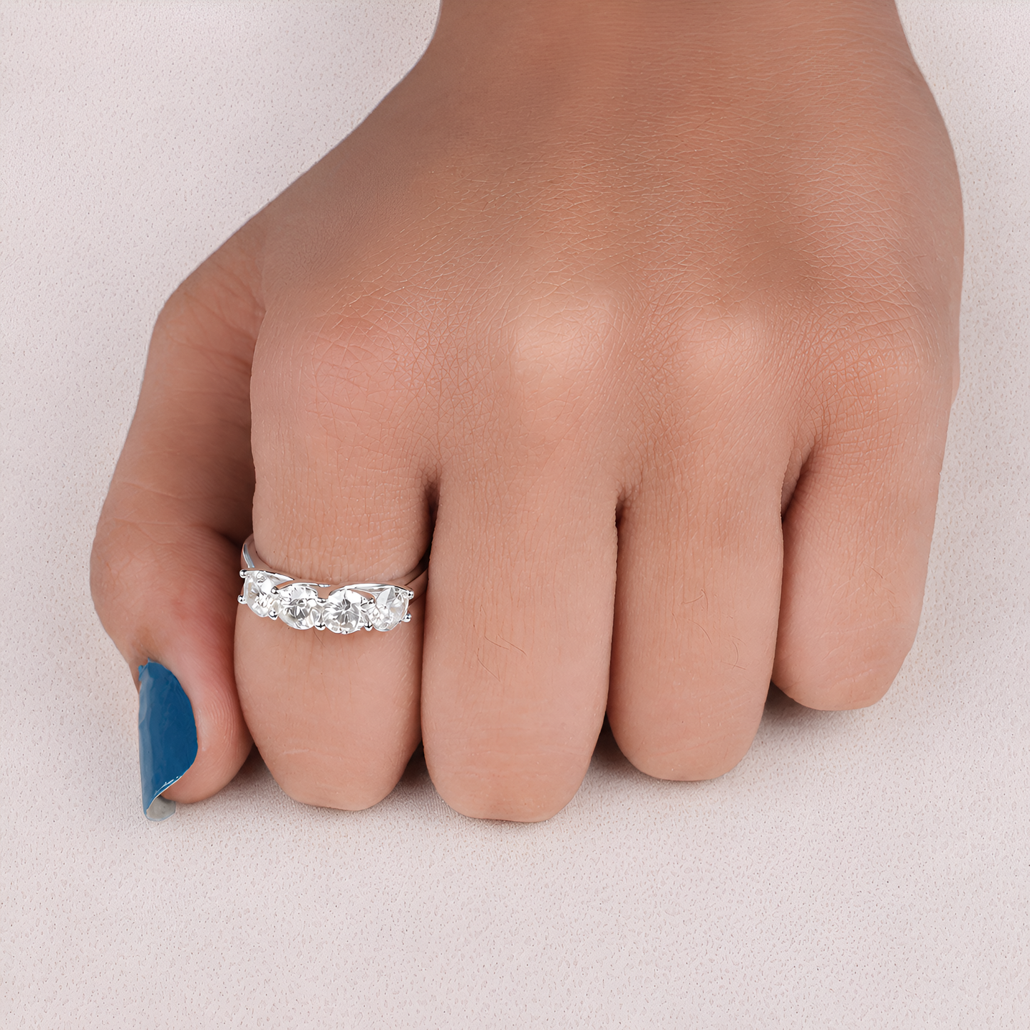 A silver ring with three round-cut clear gemstones set on a person's ring finger, shown against a light neutral background.