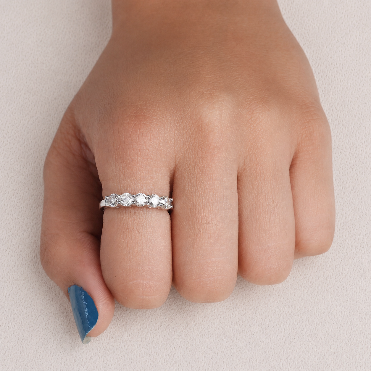A silver band ring with a row of clear round-cut gemstones worn on a person's ring finger, shown against a light neutral background.