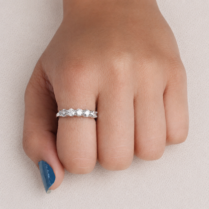 A silver band ring with a row of clear round-cut gemstones worn on a person's ring finger, shown against a light neutral background.