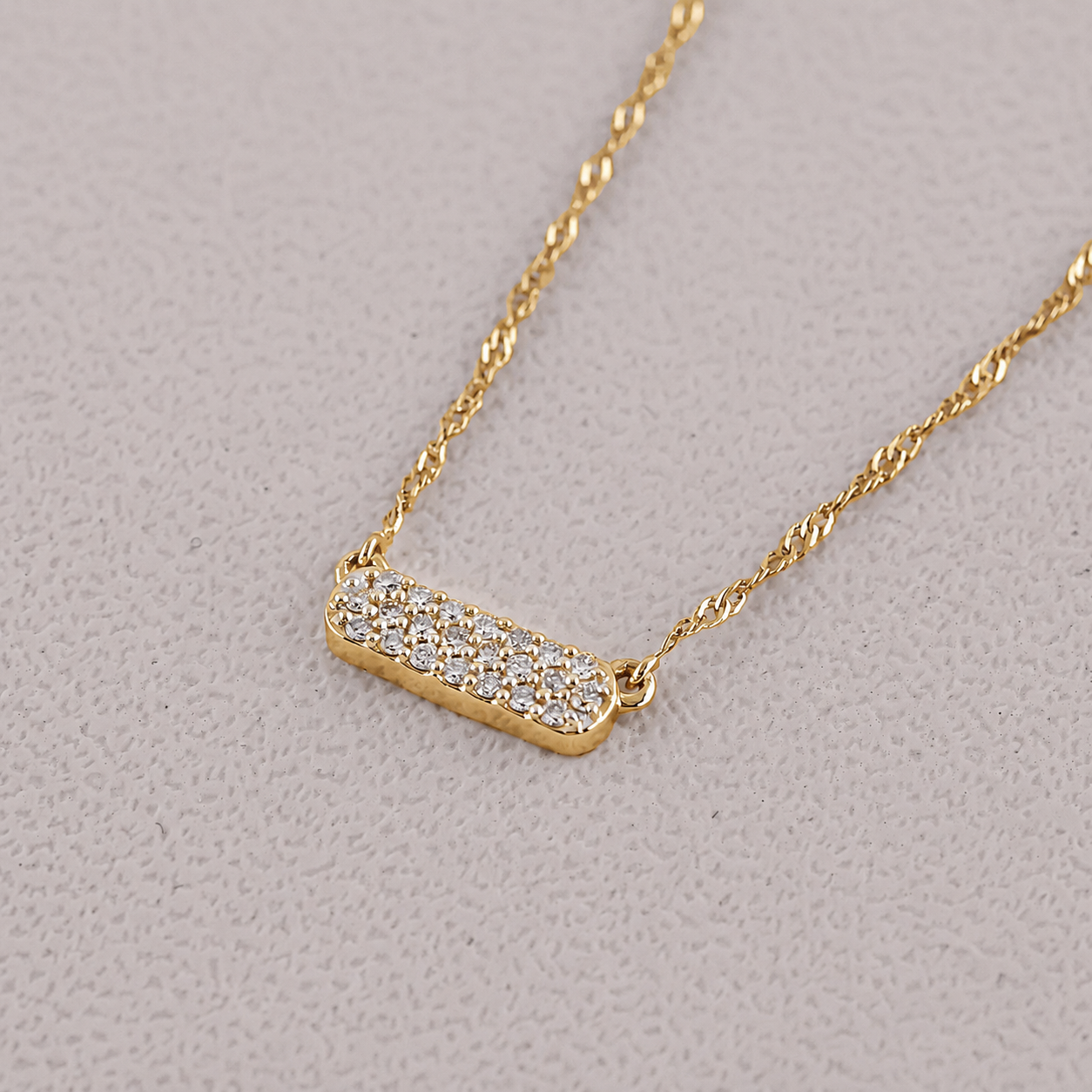 Gold necklace with a bar pendant on a light gray background