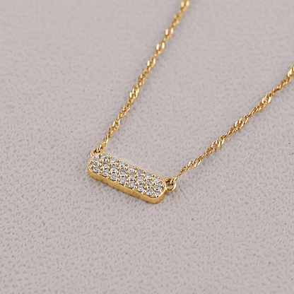 Gold necklace with a bar pendant on a light gray background