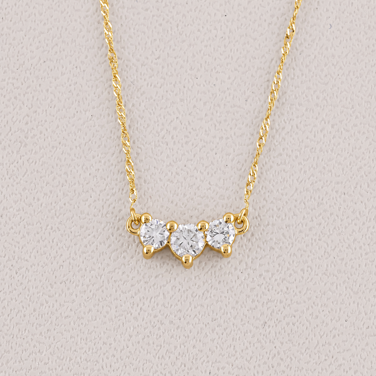 Gold necklace with heart-shaped diamond pendants on a light gray background