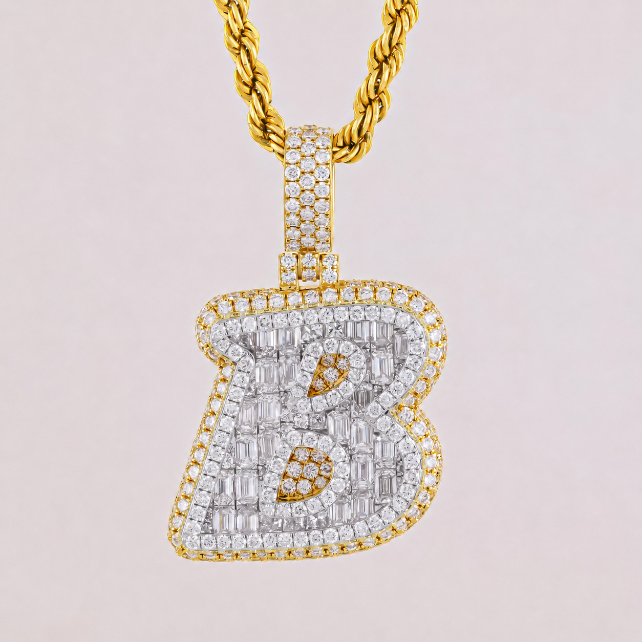 Gold necklace with a diamond-encrusted 'B' pendant on a light pink background
