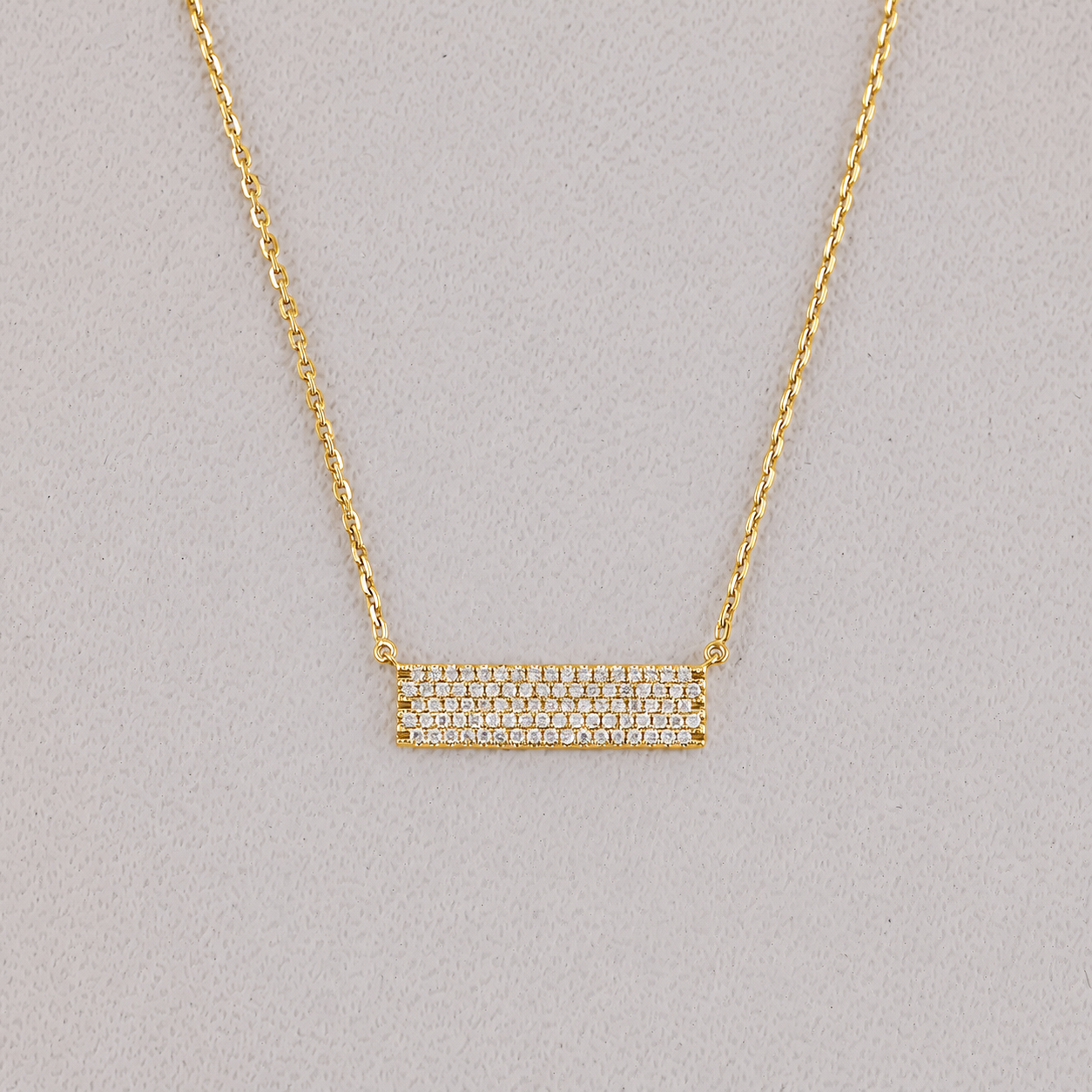 Gold necklace with a bar pendant on a gray background