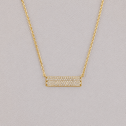 Gold necklace with a bar pendant on a gray background