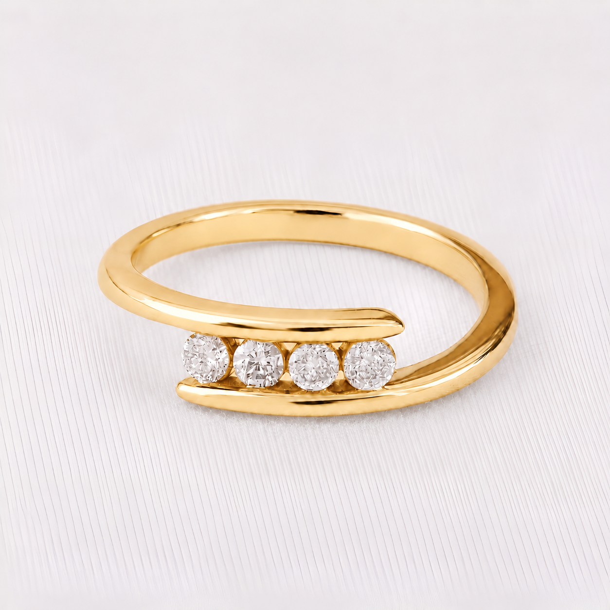 A gold open-band ring featuring four round-cut clear gemstones set across the front, displayed on a light gray textured background.