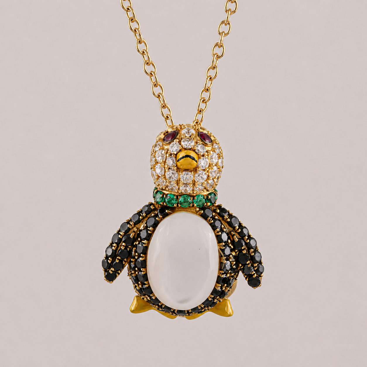 Penguin-shaped pendant with gemstones on a gold chain against a beige background