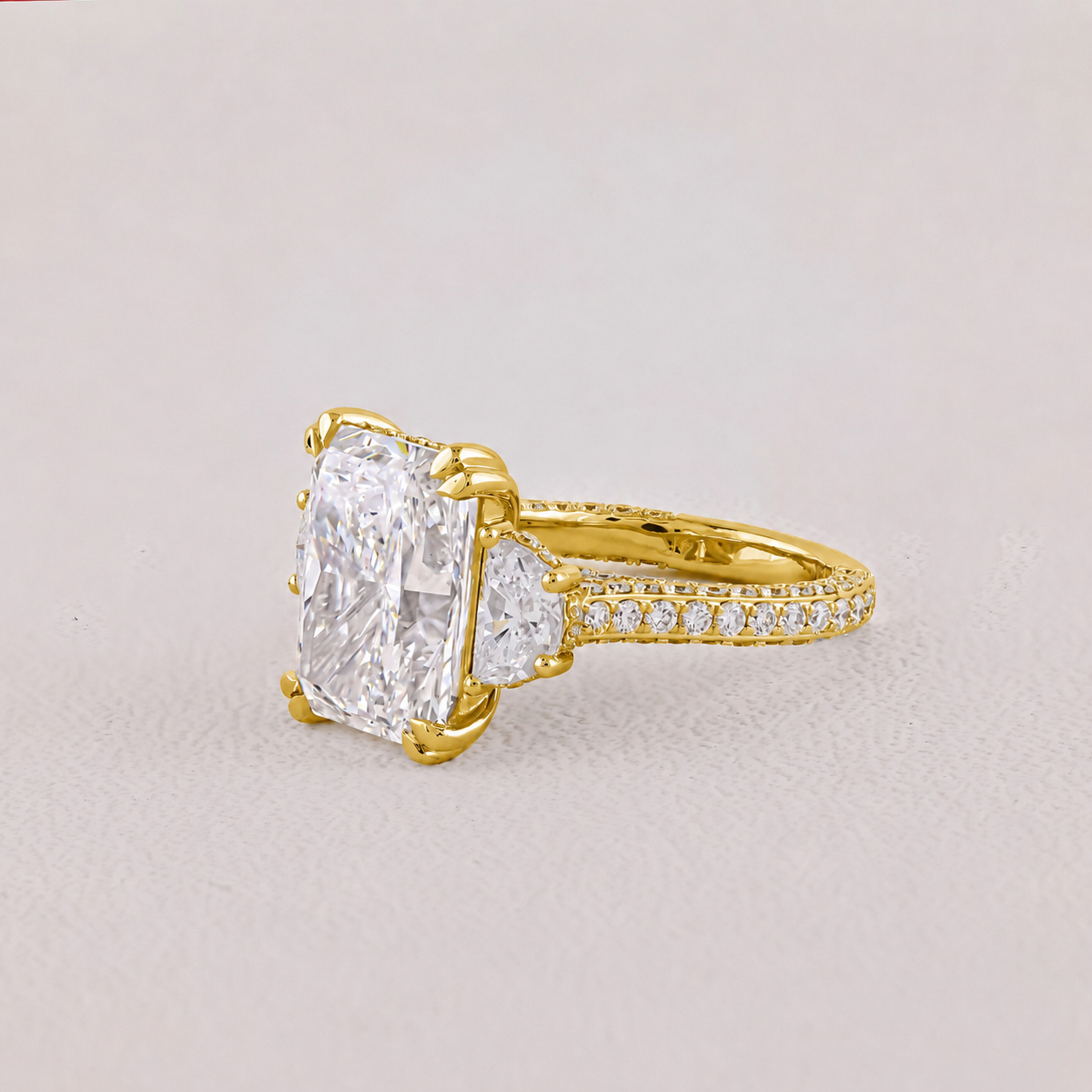 Gold ring with a large diamond and smaller diamonds on the band against a light gray background