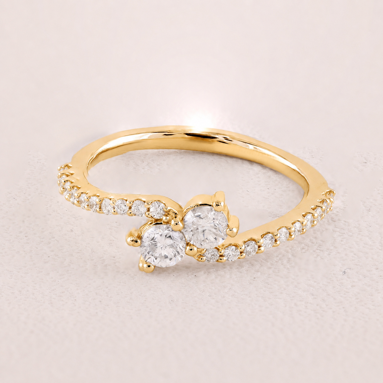 Gold ring with two prominent diamonds on a light beige background