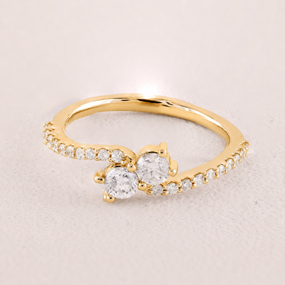 Gold ring with two prominent diamonds on a light beige background