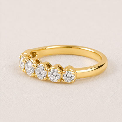 A yellow gold diamond ring with five round-cut diamonds set in a row, shown on a light beige textured background.