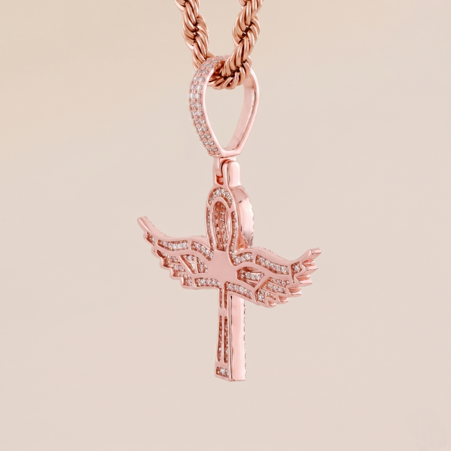 Rose gold cross pendant with wings on a beige background