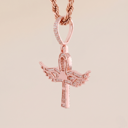 Rose gold cross pendant with wings on a beige background