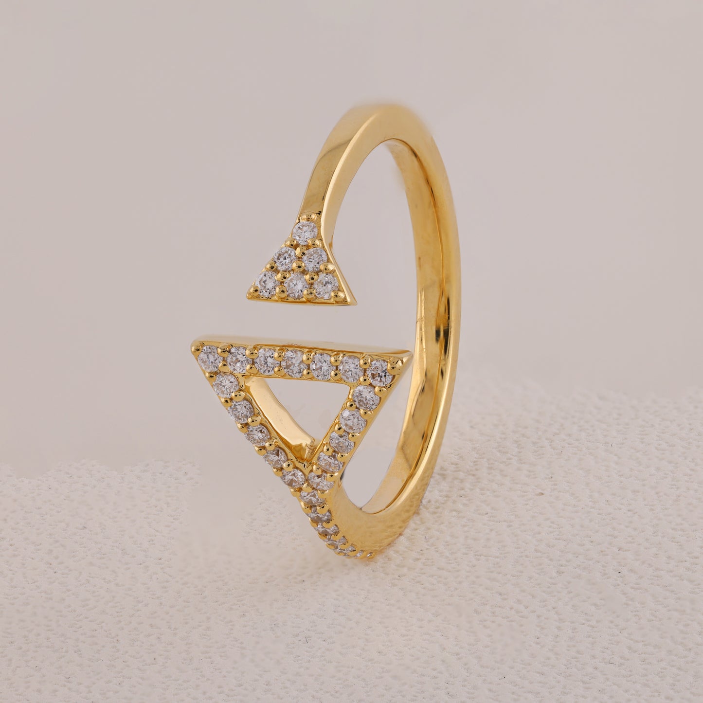Gold ring with triangular design and embedded diamonds on a beige background