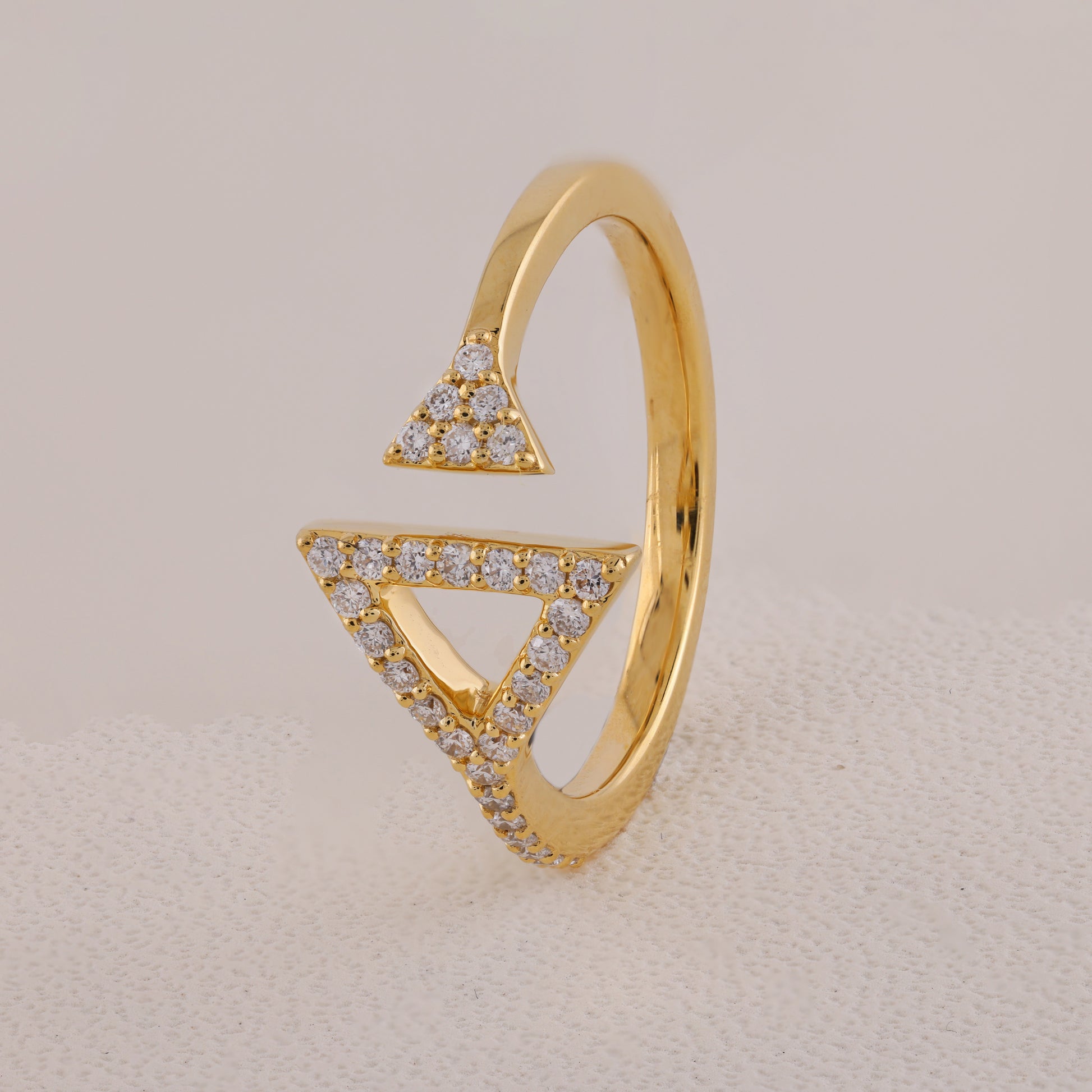 Gold ring with triangular design and embedded diamonds on a beige background