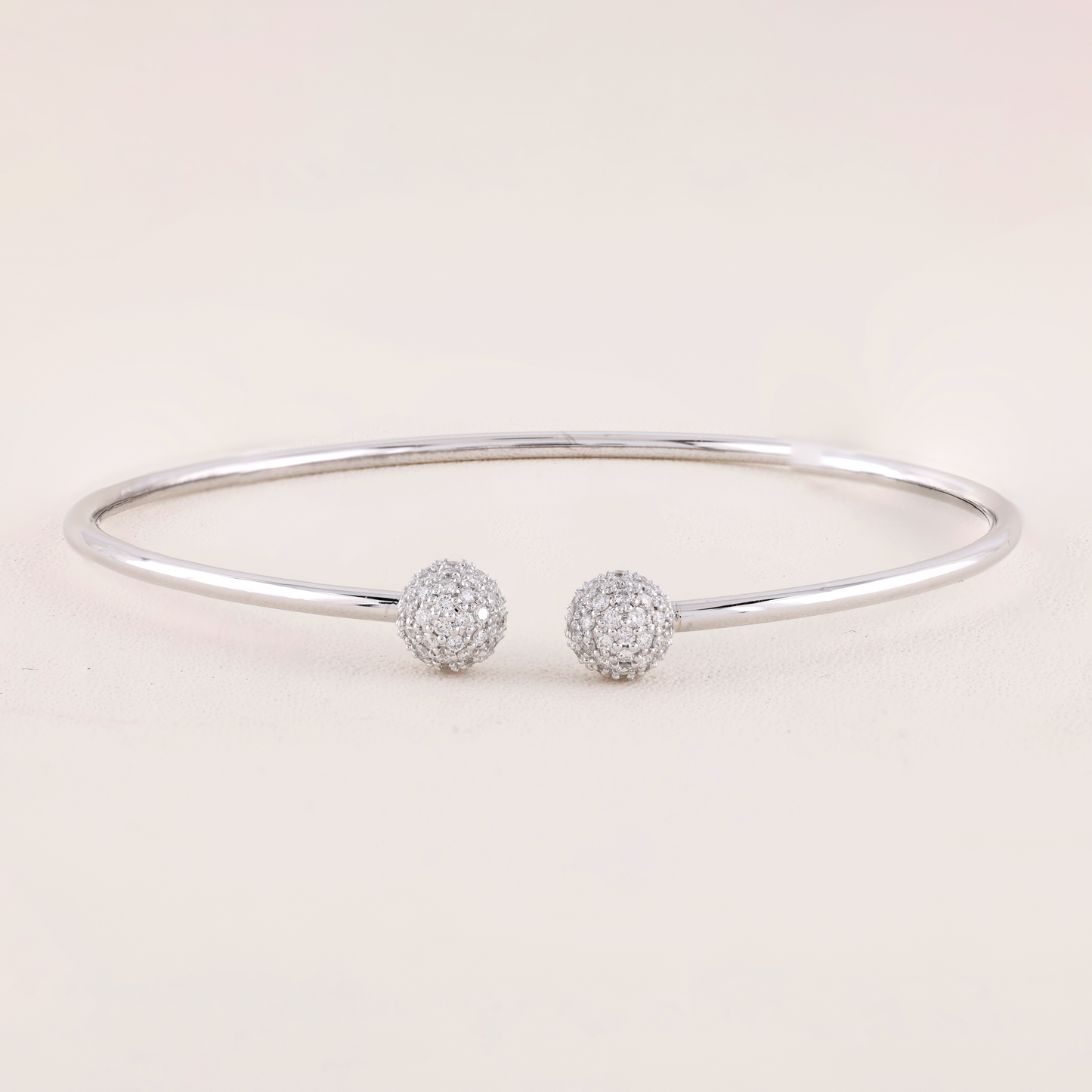 White Gold bracelet with two spherical charms on a light pink background