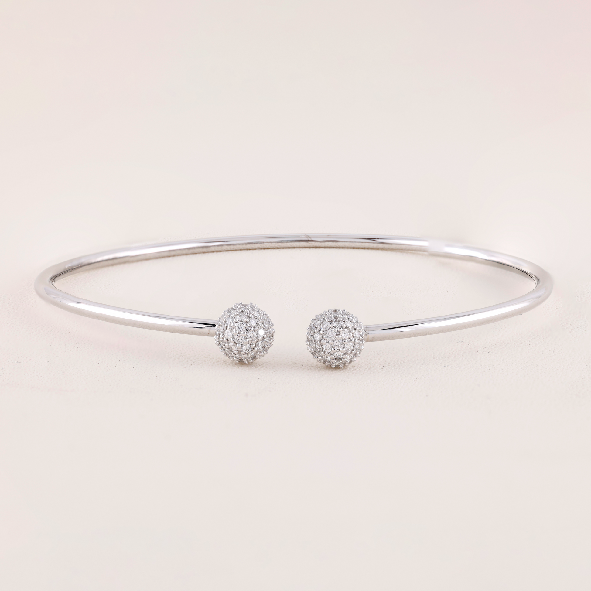 White Gold bracelet with two spherical charms on a light pink background