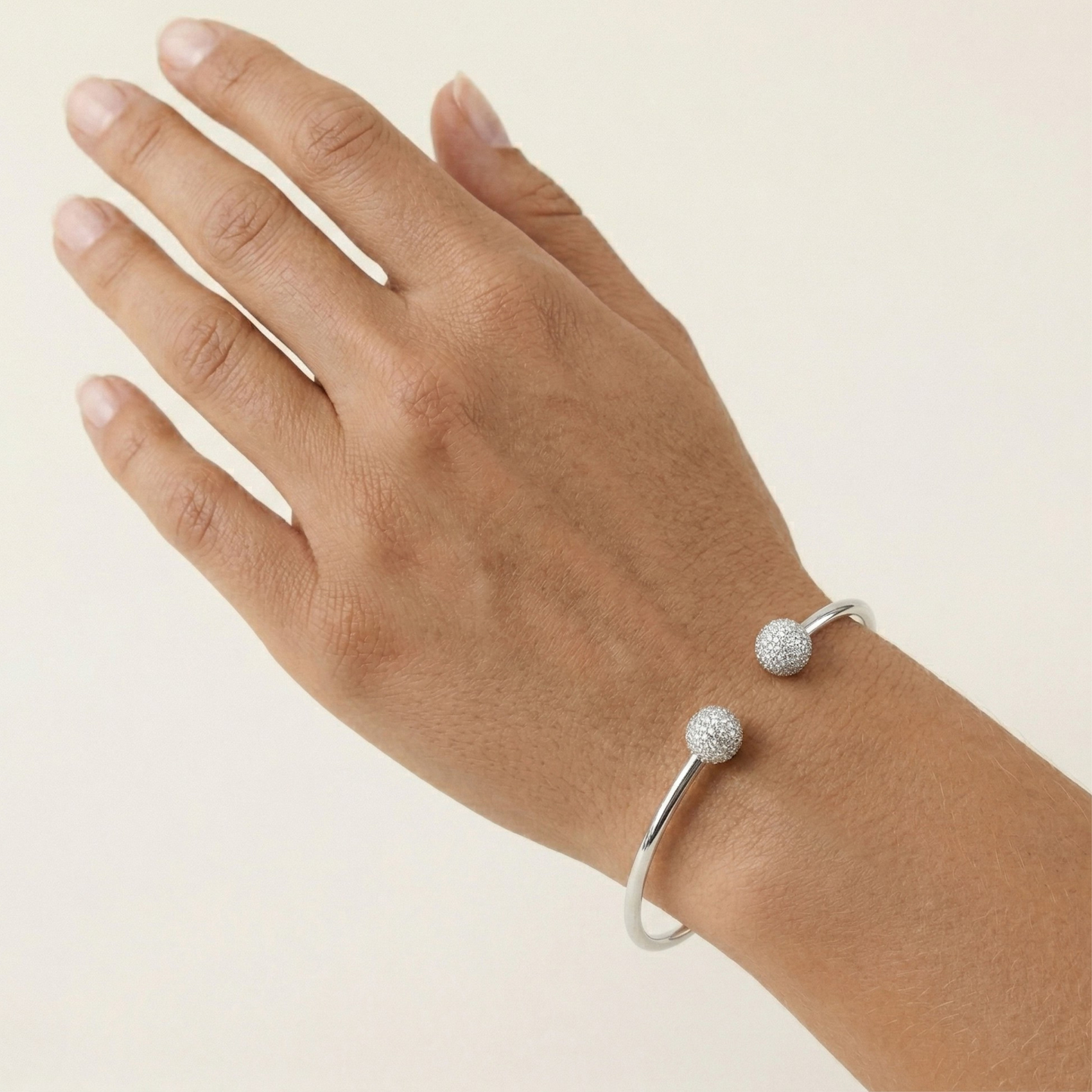 Hand wearing a silver bracelet with two spherical charms on a beige background