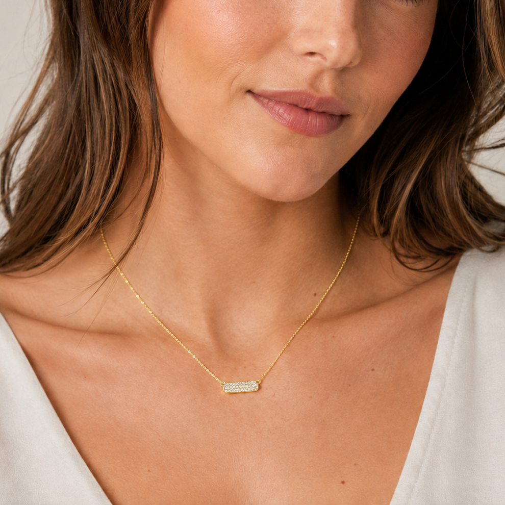 Close-up of a woman wearing a gold necklace with a bar pendant.