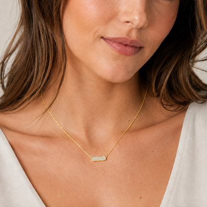 Close-up of a woman wearing a gold necklace with a bar pendant.