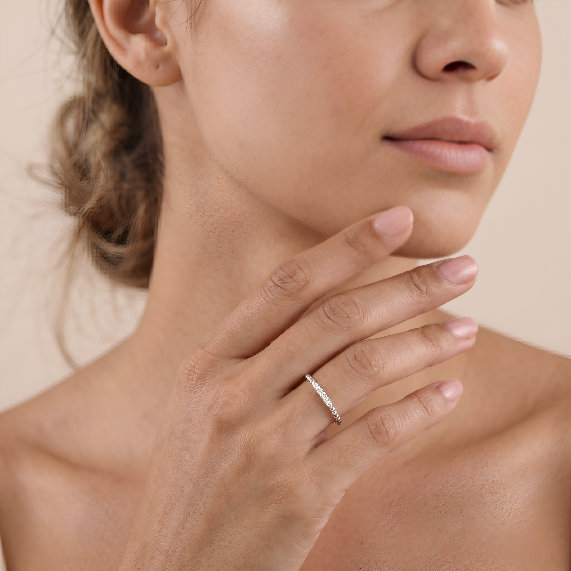 Close-up of a woman's hand wearing a diamond ring on a neutral background