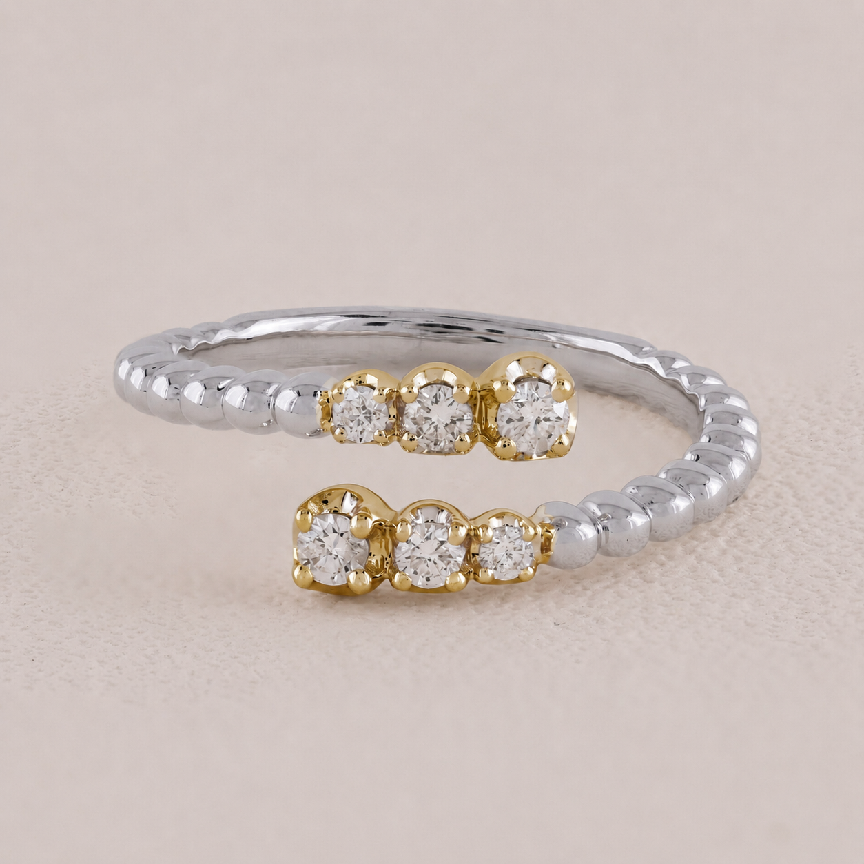 Two gold and silver open rings with diamond-like stones on a beige background