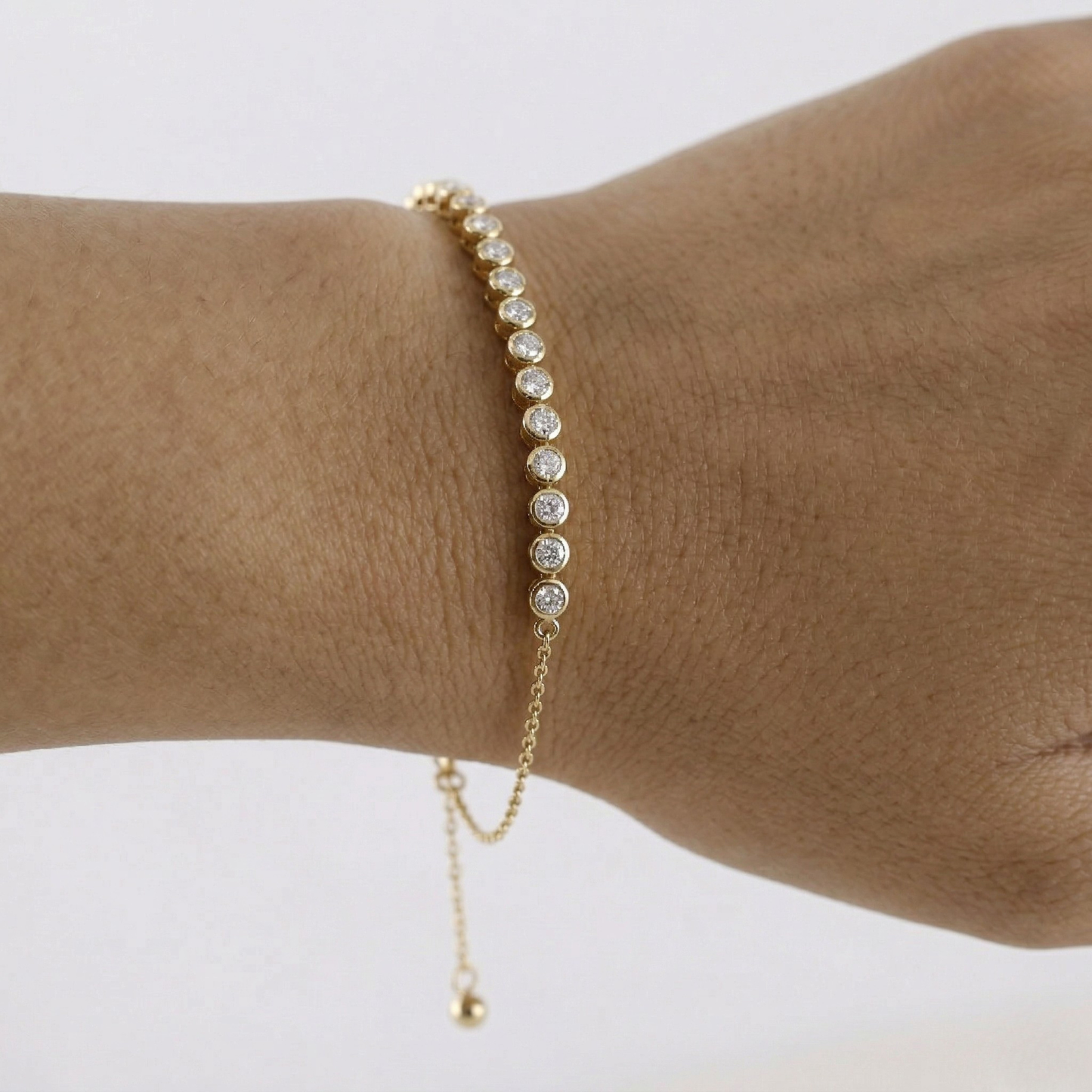 Gold bracelet with small beads on a wrist against a white background