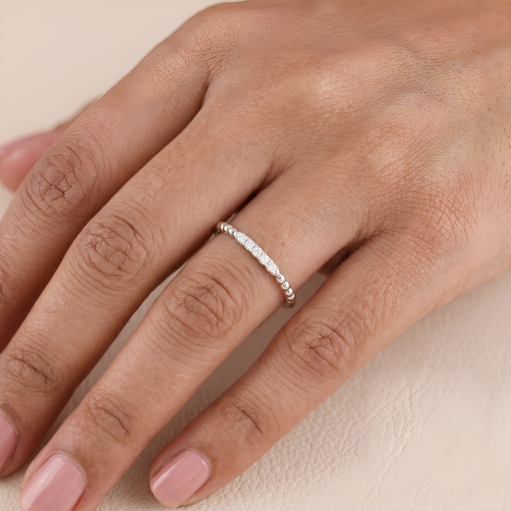 Close-up of a hand wearing a silver ring on a beige background