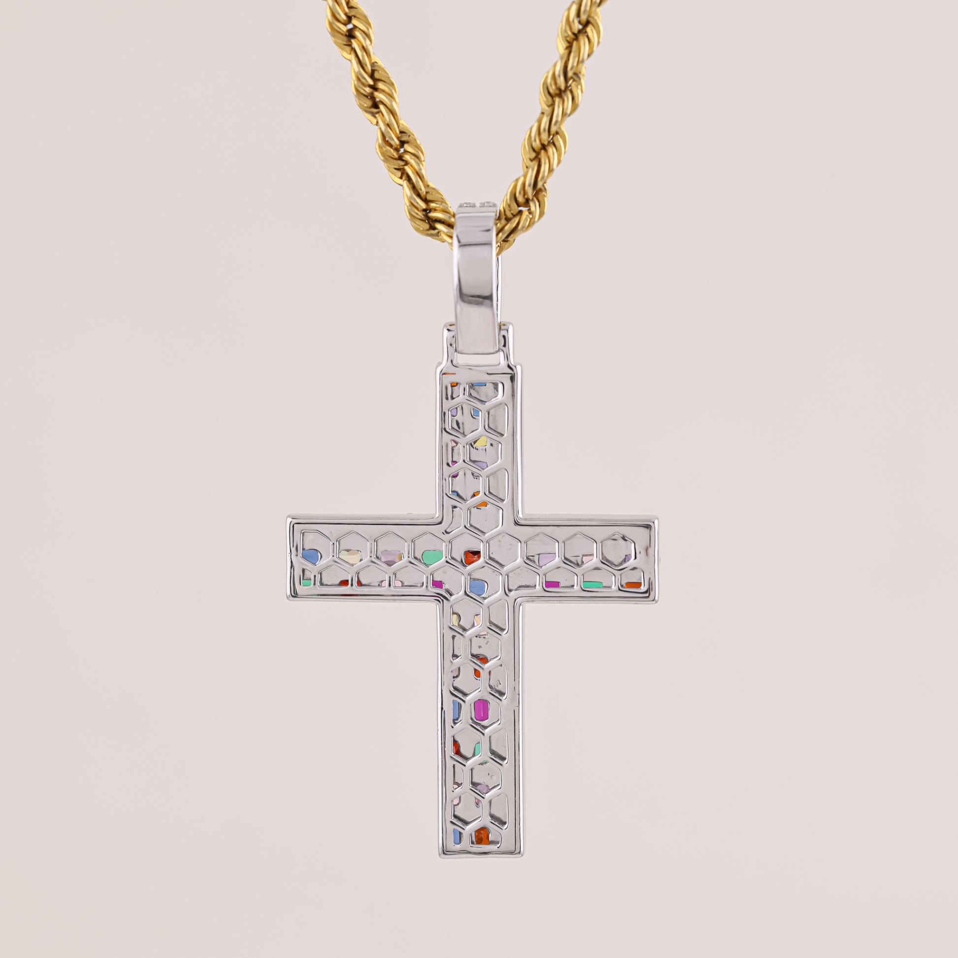 Cross-shaped pendant with colorful stones on a gold chain against a beige background