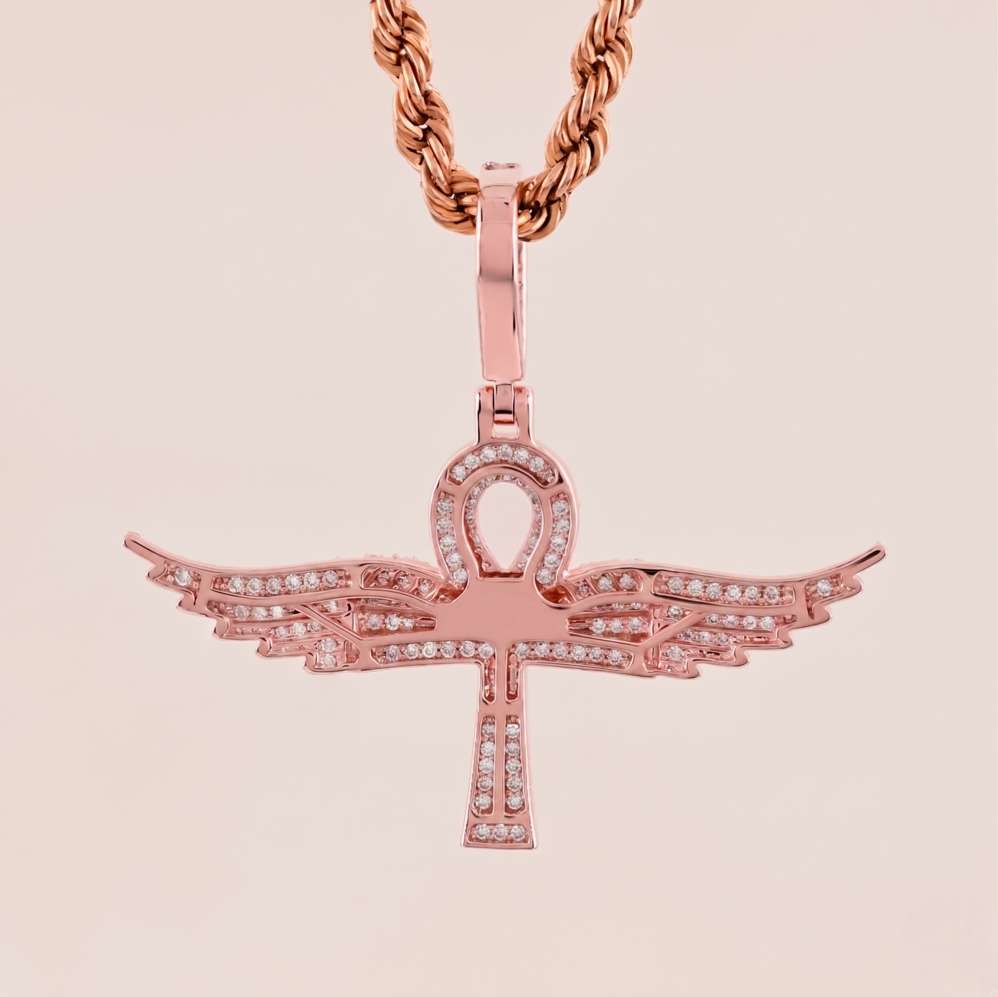 Rose gold pendant with wings on a beige background