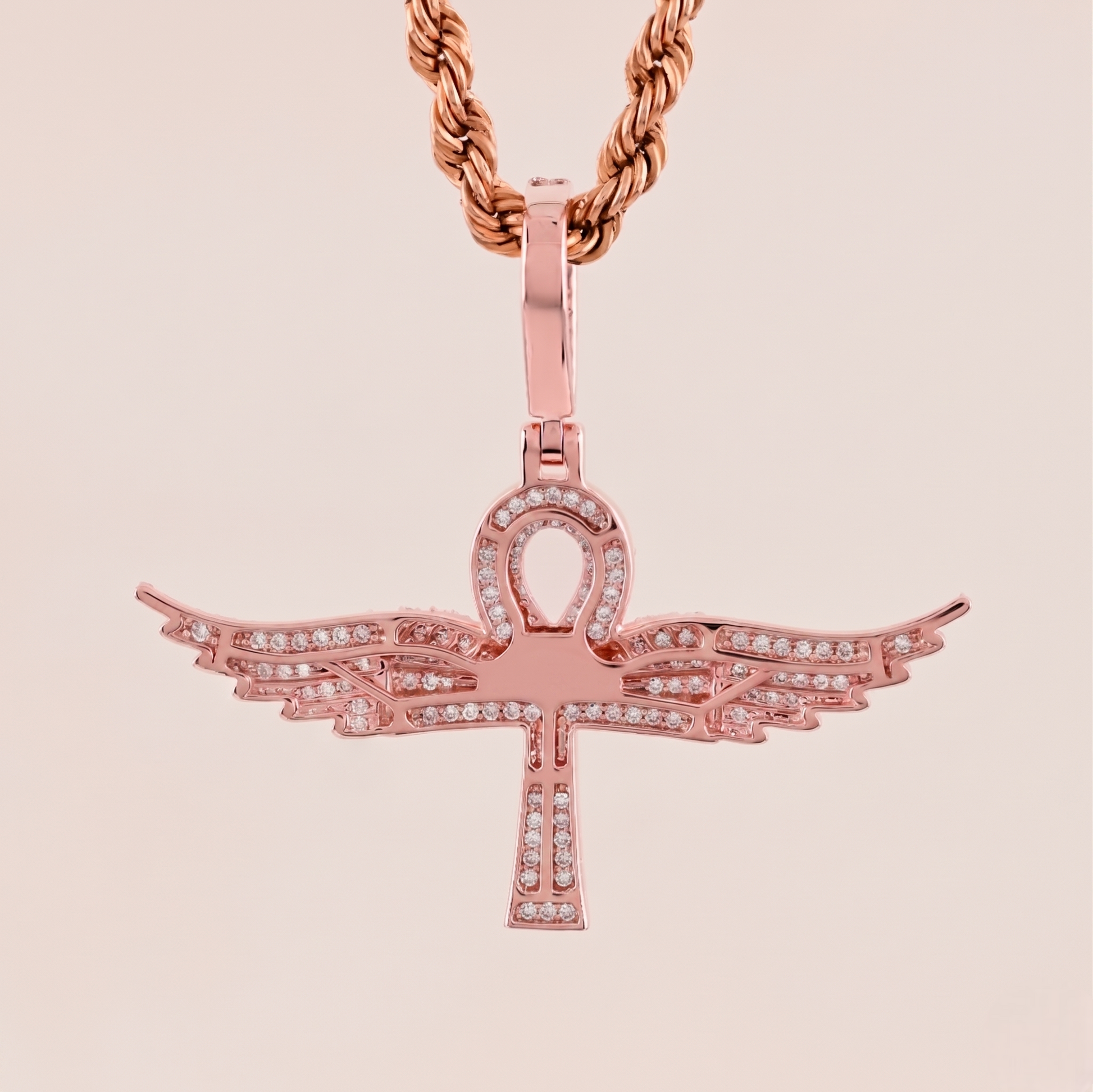Rose gold pendant with wings on a beige background