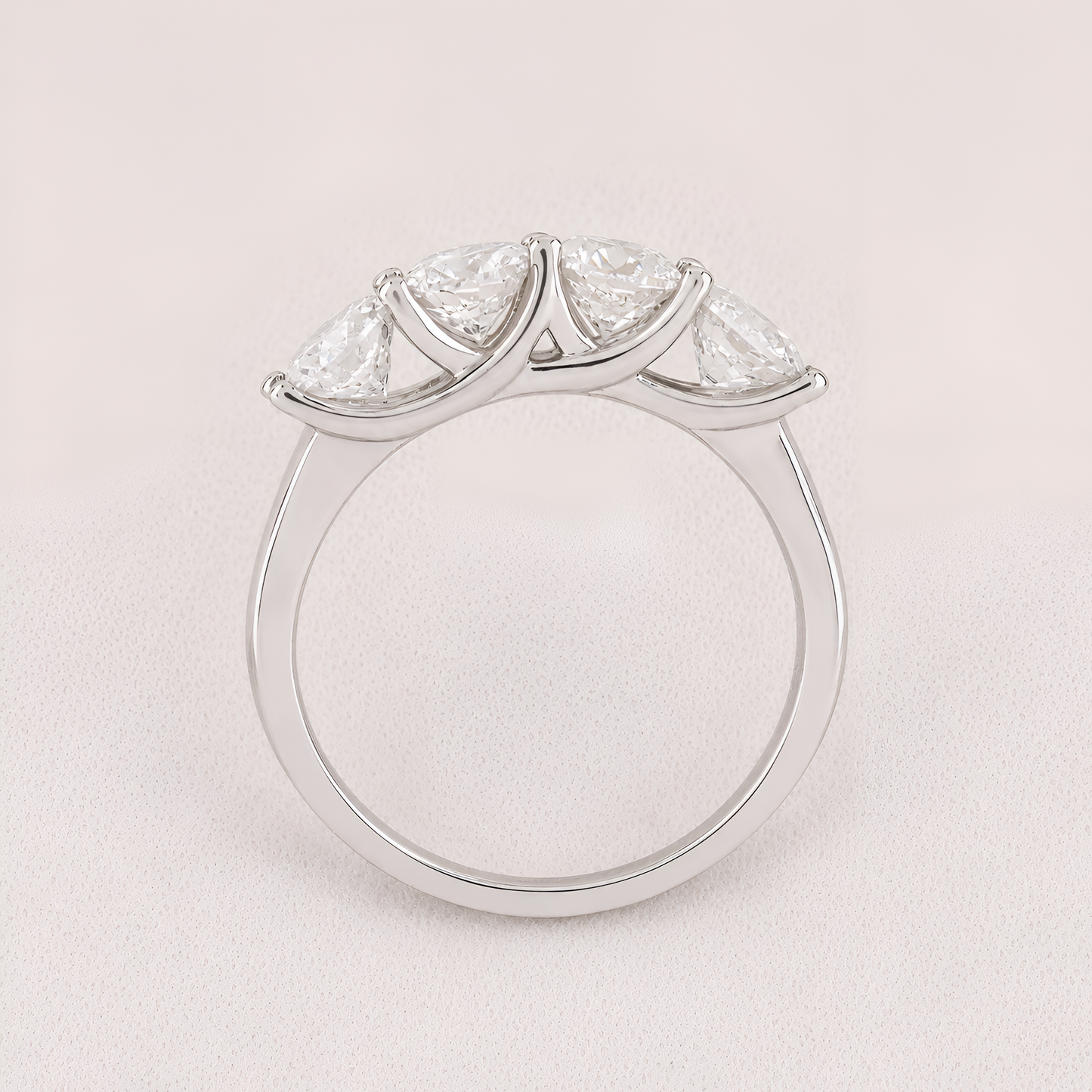 A silver three-stone diamond ring with marquise-cut diamonds set in a curved crown-like arrangement on a polished band, shown against a light pink background.
