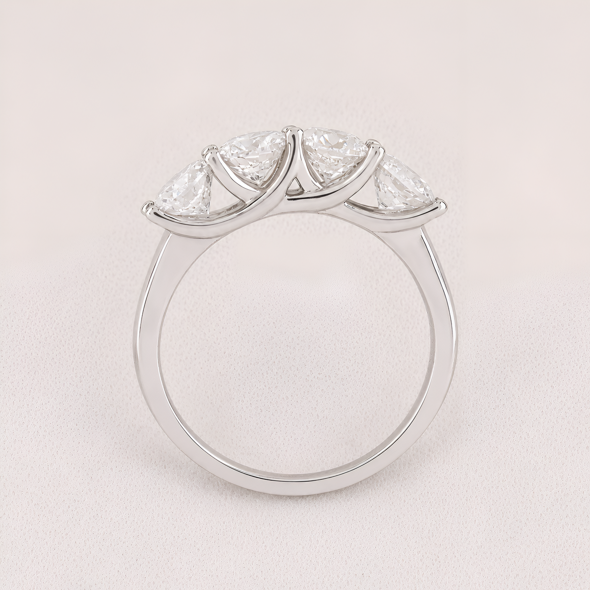 A silver three-stone diamond ring with marquise-cut diamonds set in a curved crown-like arrangement on a polished band, shown against a light pink background.