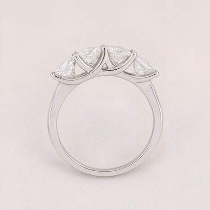 A silver three-stone diamond ring with marquise-cut diamonds set in a curved crown-like arrangement on a polished band, shown against a light pink background.
