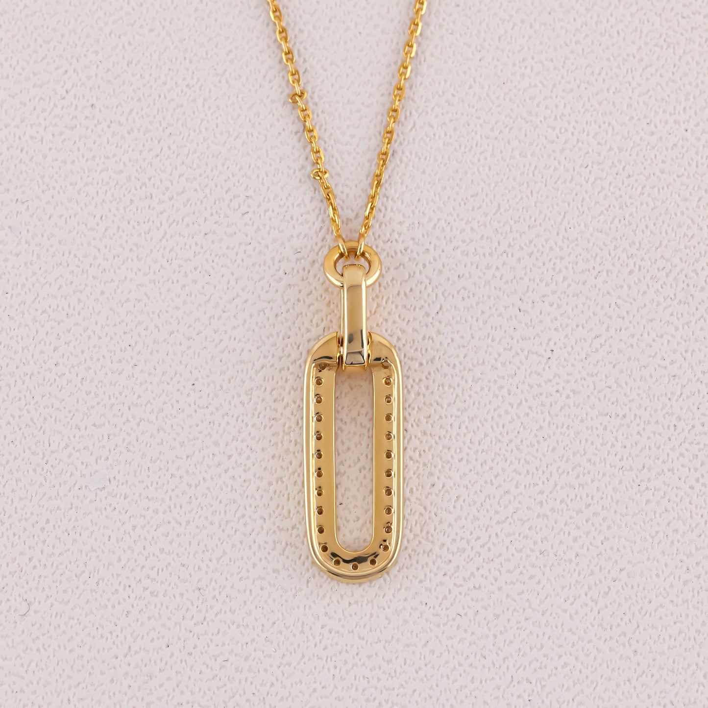 Gold necklace with a rectangular pendant on a light gray background