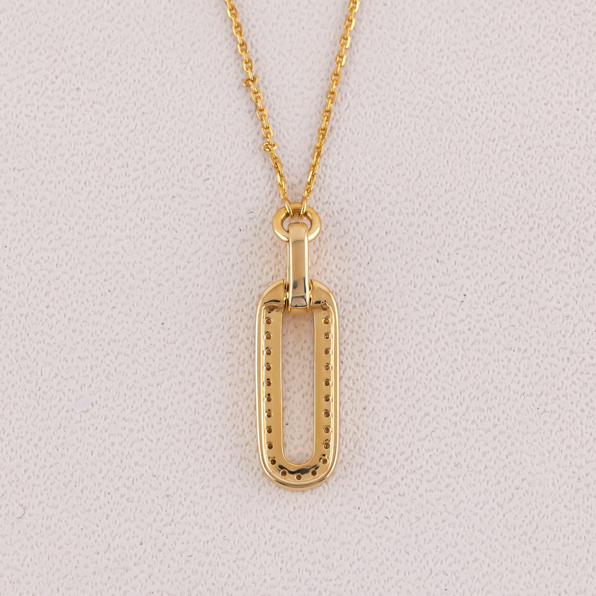 Gold necklace with a rectangular pendant on a light gray background