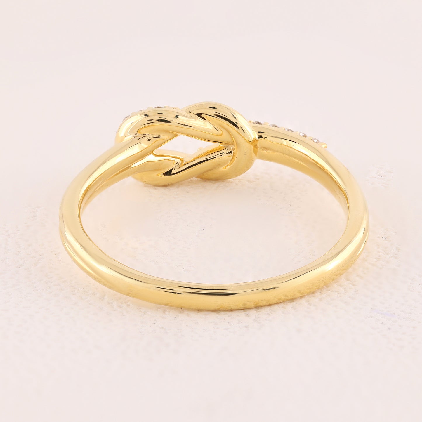 Gold knot ring on a light beige background