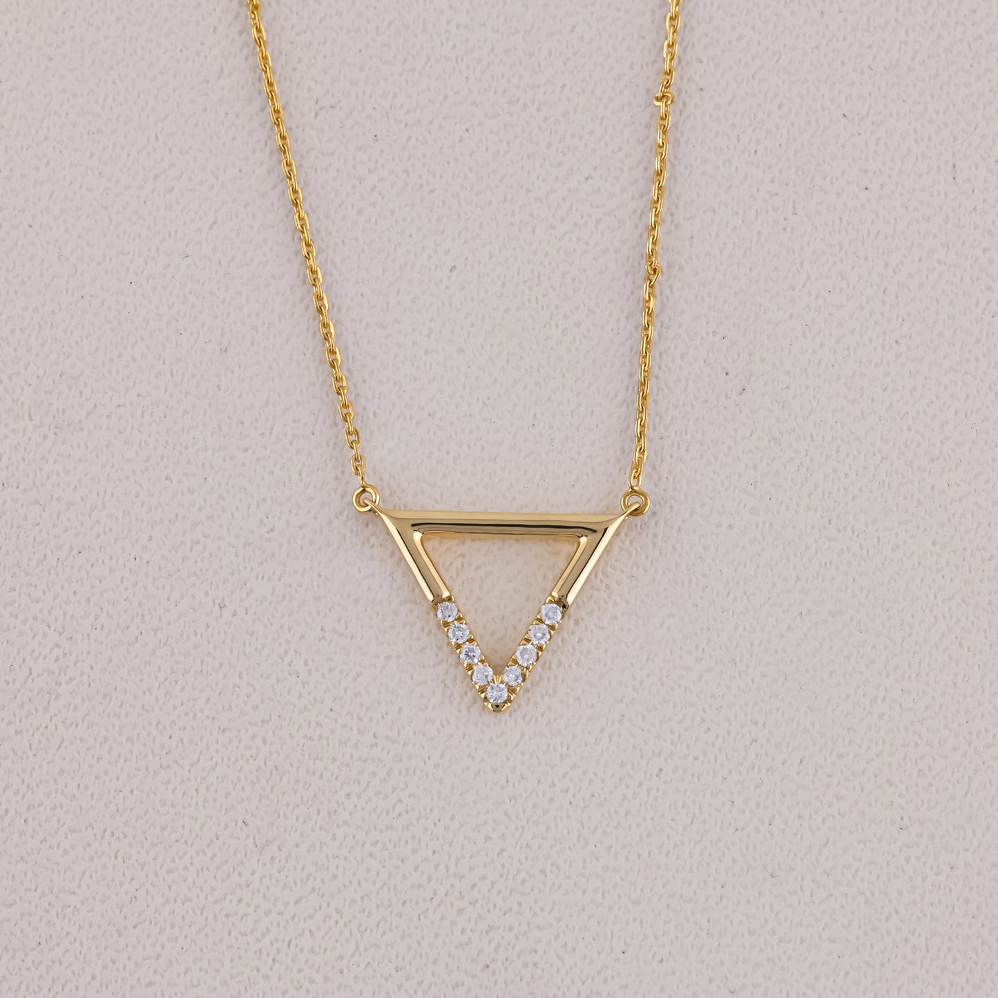 Gold necklace with a triangle pendant on a light gray background