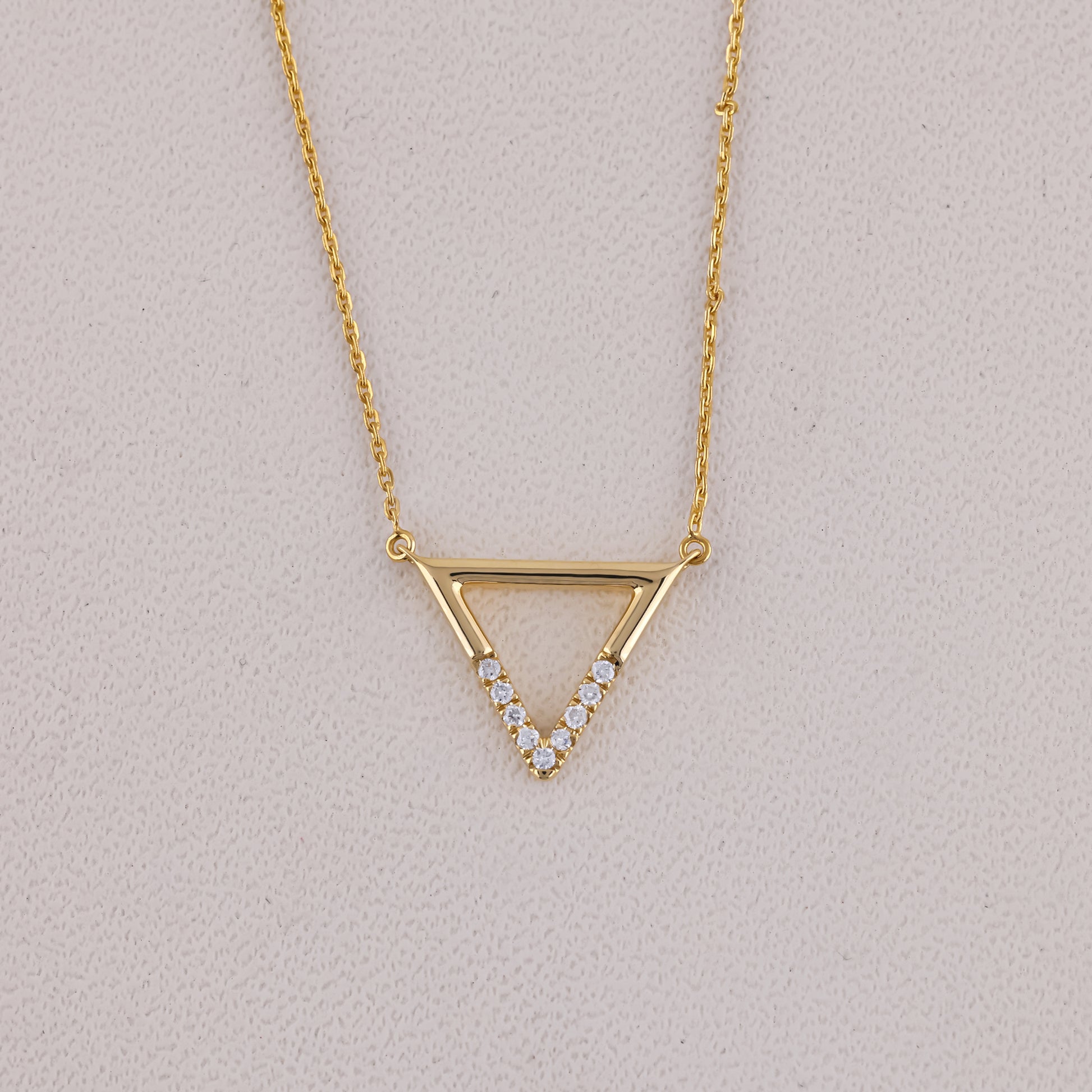 Gold necklace with a triangle pendant on a light gray background