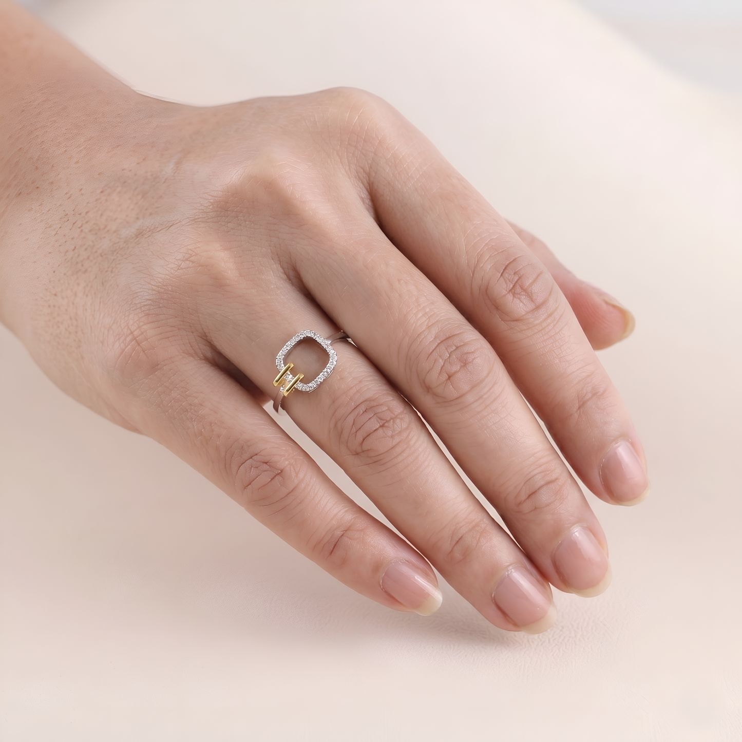 Hand wearing a silver ring with a gold accent on a light background
