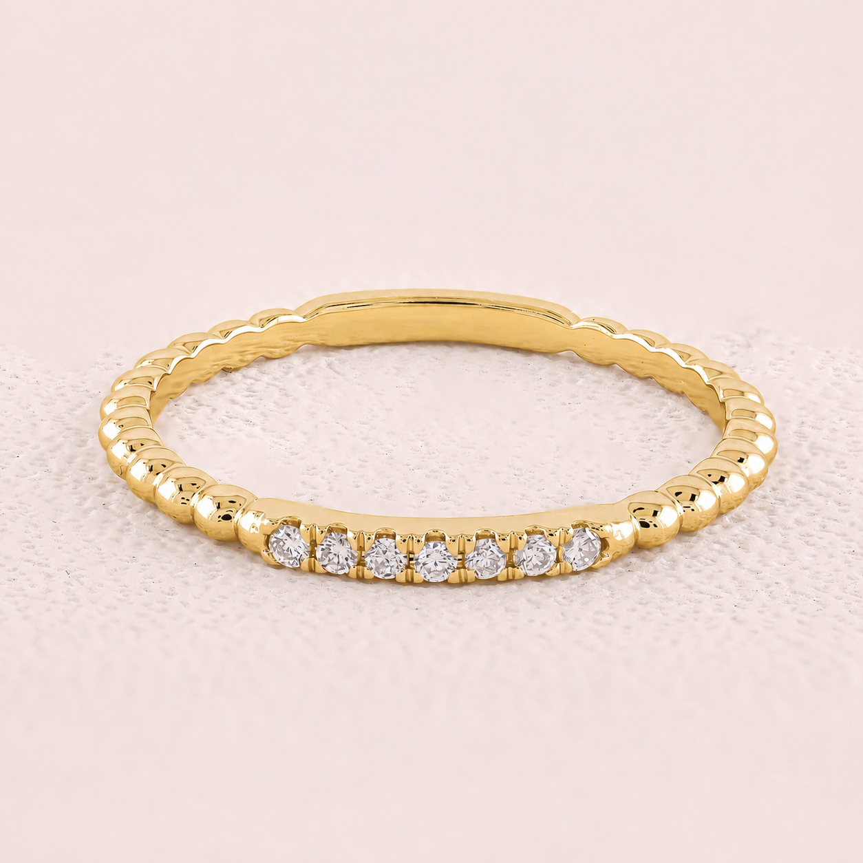 Gold ring with small diamonds on a light pink background