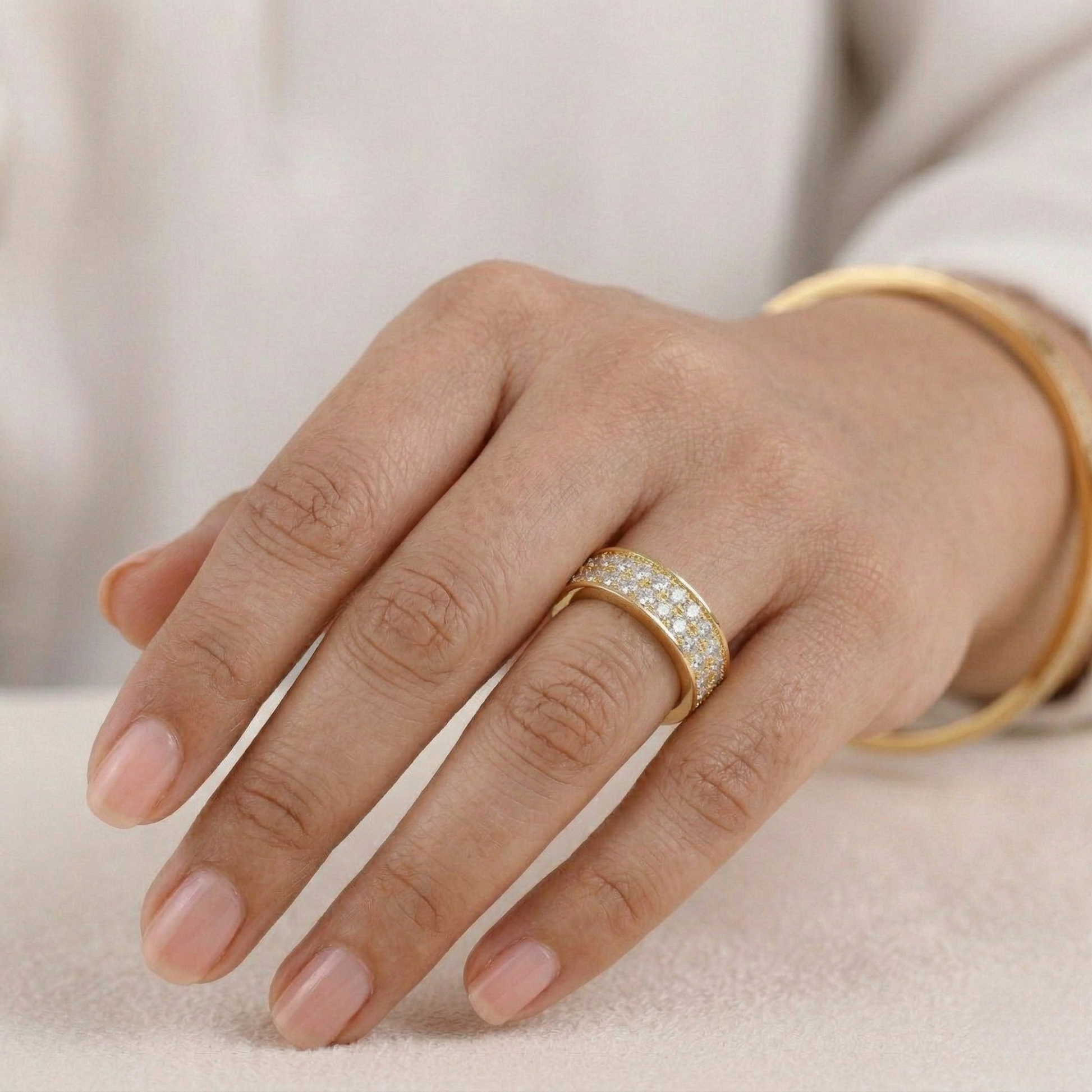Hand wearing a gold ring with diamonds on a neutral background